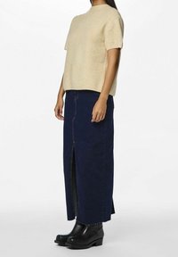 Beżowy dzianinowy top z krótkimi rękawami w połączeniu z ciemnoniebieską spódnicą dżinsową z przednim rozcięciem i czarnymi botkami. Gładkie faktury, casualowy styl.