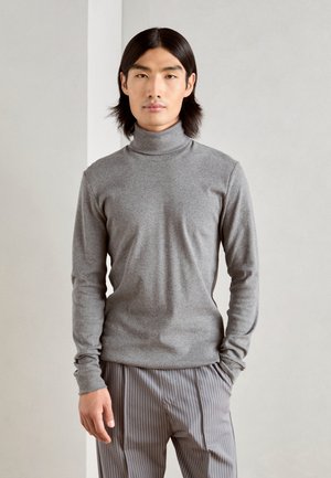 Grijze coltrui van zacht materiaal, met lange mouwen en een getailleerde pasvorm, gecombineerd met verticaal gestreepte broeken.