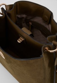 Borsa in suede verde oliva con fodera marrone, dotata di chiusura metallica, accessori in oro e forma strutturata. Inclusi taschini interni.