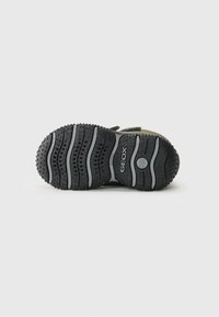 Suela de zapato de goma negra con surcos texturizados y agujeros de ventilación para mayor transpirabilidad, con un logo circular y acentos en gris.