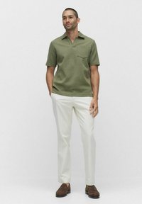 Vihreä oliivinvärinen lyhythihainen paita, jossa on kaulus ja tasku, yhdistettynä valkoisiin slim-fit-housuihin ja ruskeisiin kenkiin.