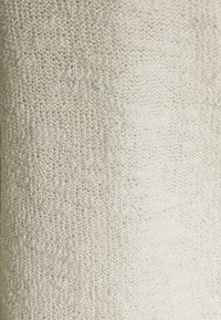 Texturerat krämfärgad tyg med en mjuk, stickad yta, som har ett subtilt mönster och en något varierande ytdjup.