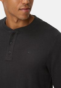 Sort langærmet henley skjorte lavet af ribbet stof, med rund krave, tre-knap lukning og et diskret logo på brystet.