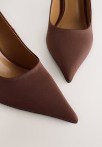 Rudos, smailių priekių aukštakulniai, pagaminti iš lygaus audinio. Turi elegantišką siluetą su minimalistiniu dizainu ir subtilų blizgantį pado apdailą.