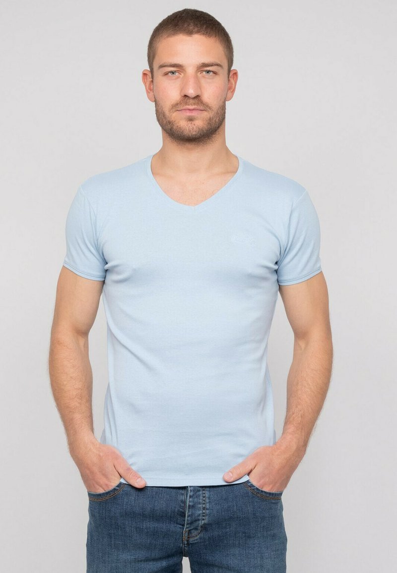 T-shirt V en jersey bleu clair dans un tissu doux et extensible. Design ajusté avec des manches courtes et un logo discret sur la poitrine. Porté avec un jean en denim.