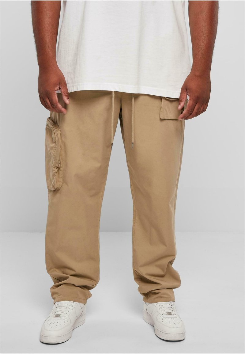Beige Cargo-Hosen aus Baumwolle mit elastischem Bund und Kordelzug. Verfügt über Seitentaschen und eine lässige Passform. Kombiniert mit weißen Sneakern.
