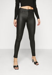 Jeans skinny de talle alto en negro, confeccionados con un material liso y elástico, con un acabado elegante. Cuenta con un cierre de botón y cremallera en la parte frontal.