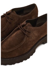 Men’s dark brown suede lace-up shoes with thick, textured soles and rounded toes, shown in close-up detail.