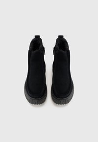 Bottines noires avec un extérieur en daim lisse, doublure en fourrure, fermeture éclair et une semelle en caoutchouc épaisse et texturée.