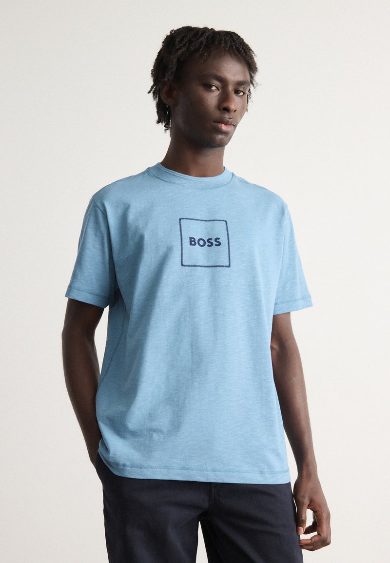 Camiseta de algodón azul claro con cuello redondo y mangas cortas. Presenta un logo cuadrado bordado en marino "BOSS" en el pecho.