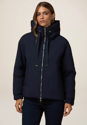 Veste rembourrée bleu marine avec un col montant, une capuche à cordon de serrage et une fermeture éclair. Comprend des poignets élastiques et deux poches latérales.