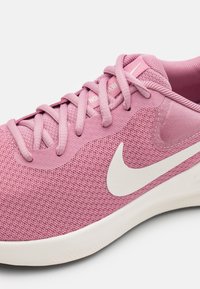 Chaussure de sport rose clair avec tige en mesh, lacets plats et logo swoosh blanc. Présente une semelle lisse et durable ainsi qu'un col rembourré.