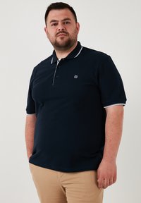 Námornícka polo košeľa s golierom a tromi gombíkmi, s bielymi akcentmi na golieri a rukávoch, vyrobená z textúrovanej bavlnenej látky.