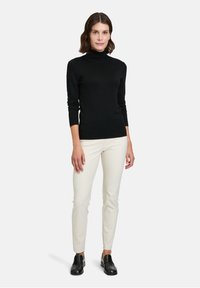 Schwarzer Rollkragenpullover, lange Ärmel, taillierte Passform; kombiniert mit cremefarbenen Slim-Fit-Hosen und schwarzen Slippern. Minimalistischer Stil, neutrale Farben.