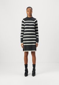 Robe en tricot avec des rayures noir et blanc, col rond, manches longues, texture côtelée et fentes sur les côtés à l'ourlet.