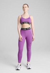 Conjunto de sujetador deportivo y leggins morados hecho de una tela elástica. El sujetador cuenta con tirantes finos y una banda negra con logo; los leggins tienen un ajuste aerodinámico.