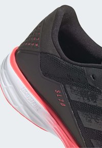 Scarpa sportiva nera con tomaia testurizzata, presenta dettagli rosa, una suola bianca con "LIGHTSTRIKE" in rilievo e fori di ventilazione sul tallone.