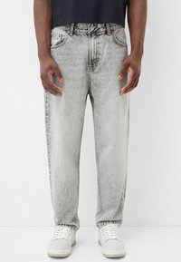 Jeans grigi chiari a gamba dritta con una finitura sbiadita, cinque tasche, passanti per cintura e hardware argentato, indossati con sneakers bianche.