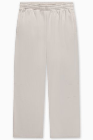 Svijetlo bež trenirka s elastičnim pojasom, dva bočna džepa i suptilnim detaljima šavova na nogavicama. Glatka tekstura tkanine.