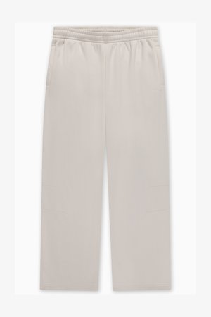 Svijetlo bež trenirka s elastičnim pojasom, dva bočna džepa i suptilnim detaljima šavova na nogavicama. Glatka tekstura tkanine.