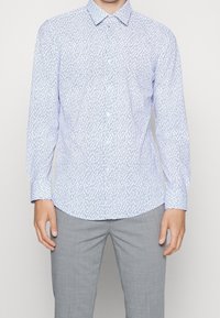 Camisa azul claro abotonada con un diseño estampado que presenta líneas verticales. Manga larga, corte entallado, con cuello clásico.