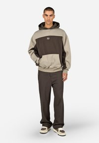 Hættetrøje i brunt og beige farveblok design med frontlomme, parret med mørke bukser og flerfarvede fodtøj.