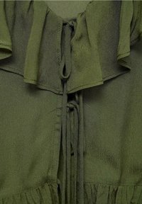 Olivenfarbener Stoff mit einem Rüschenausschnitt und einer vorderen Bindung, die aus dünnen Stoffbändern besteht.