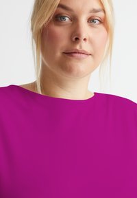 Fuchsia Kurzarmoberteil mit Rundhalsausschnitt, glatter Textur und dezentem Glanz. Minimalistisches Design, zugeschnitten auf eine lockere Passform.