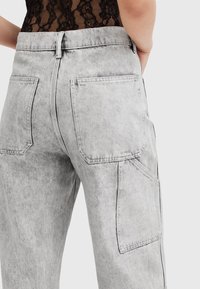 Pantalones cargo de mezclilla gris con una cintura alta, grandes bolsillos traseros y una textura desgastada con costuras en contraste.