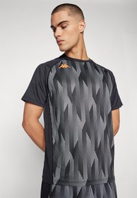 Black athletic t-shirt featuring a striped pattern in white and gray. Includes an orange logo on the upper left side and short sleeves.