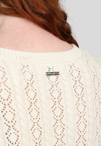 Pull en maille crème avec un motif délicat en échelle et en diamant, un col côtelé et une petite étiquette de marque près du col arrière.