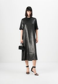 Abito midi metallizzato nero con maniche corte e vestibilità morbida. Abbinato a tacchi neri con fasce e una piccola borsa strutturata.