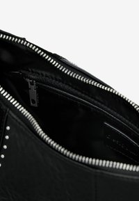Interieur van een zwarte, getextureerde leren tas met een ritszak en zilverkleurige ritsdetails langs de rand.