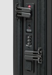 Dettaglio della cerniera di una valigia nera con doppie serrature TSA, quadranti a combinazione e una porta di ricarica USB. Tessuto strutturato visibile intorno agli accessori.