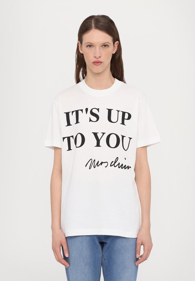 Vit bomull t-shirt med bold svart text som lyder "DET ÄR UPP TILL DIG" och en handskriven signatur. Avslappnad passform med korta ärmar.