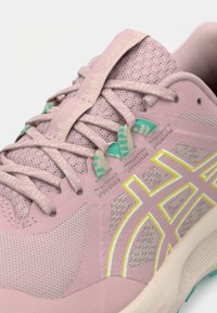 Jasnoróżowe buty sportowe wykonane z siateczki i materiałów syntetycznych. Posiadają zielone akcenty, teksturowane sznurówki i wzorzystą cholewkę.