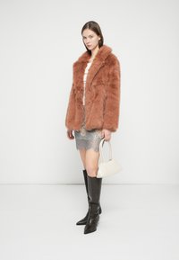 Παλτό από ψεύτικη γούνα σε χρώμα σκουριάς με φαρδύ γιακά, συνδυασμένο με μεταλλική ασημί φούστα με δαντέλα, μαύρες μπότες μέχρι το γόνατο και λευκή τσάντα χειρός.