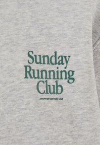 Szara koszulka z krótkim rękawem z teksturowanej tkaniny, z zielonym haftowanym napisem "Sunday Running Club" oraz "ANOTHER COTTON LAB" z przodu.