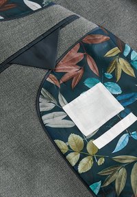Grau strukturiertem Stoff mit grün-braunem Blumenmusterbesatz. Verfügt über ein weißes quadratisches Patch und einen weißen Akzentstreifen.