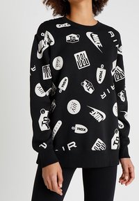 Svart sweatshirt med olika Nike-logotyper och text i vitt, med avslappnad passform, rund halsringning och ribbad mudd samt fåll.