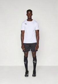 Biała sportowa koszulka z krótkim rękawem z czarnym logo, czarne szorty piłkarskie oraz czarne skarpetki sięgające uda z logo; stylowy, nowoczesny design.