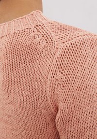 Pull en tricot rose clair avec un motif texturé, doté d'un col rond et d'un design en maille ouverte au niveau des épaules.