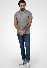 Grå polo T-shirt med korte ærmer, parret med opsmøgede blå jeans og hvide sneakers. Stoffet ser glat og bomuldsagtigt ud.