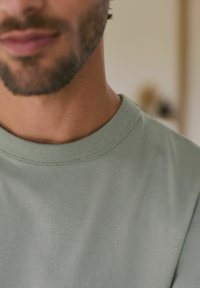 Hellgrünes Baumwoll-T-Shirt mit einem gerippten Rundhalsausschnitt. Der Stoff wirkt weich mit einer glatten Textur, minimalen Details und ohne sichtbare Muster.