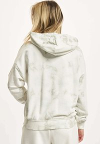 Crewneck hettegenser i lys kremfarge med en marmorert grønn tekstur. Den har hette med snøring og ribbestrikkede mansjetter, laget av mykt og koselig stoff.