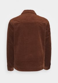 Brun kordflorsjacka med en texturerad yta, knäppte ärmmuddar och en klassisk krage, med vertikala ribbade mönster överallt.