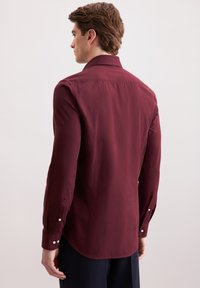 Camicia a maniche lunghe color bordeaux con colletto strutturato, polsini abbottonati, tessuto liscio e orlo curvo, vista da dietro.