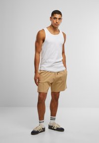 Hvit ermeless tank topp, beige shorts med snøring, svart og hvit stripete sokker, og marineblå joggesko med lyse detaljer.