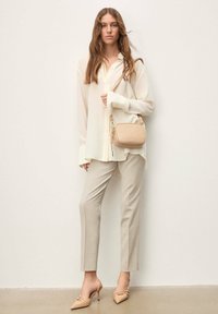 Blouse crème légère à boutons sur le devant, pantalon beige ajusté, et escarpins slingback nude. Petit sac bandoulière beige avec détail zippé.