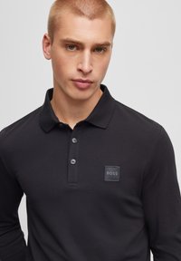 Svart långärmad polo skjorta med klassisk krage, plagg med tre knappar och en fyrkantig patch med varumärkeslogotypen. Slätt, figurnära tyg.